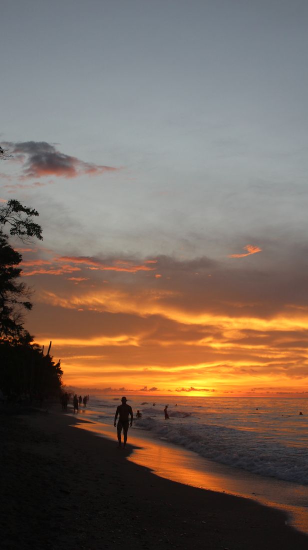 Atardecer naranja sobre el mar Caribe, con una persona caminando por la orilla.