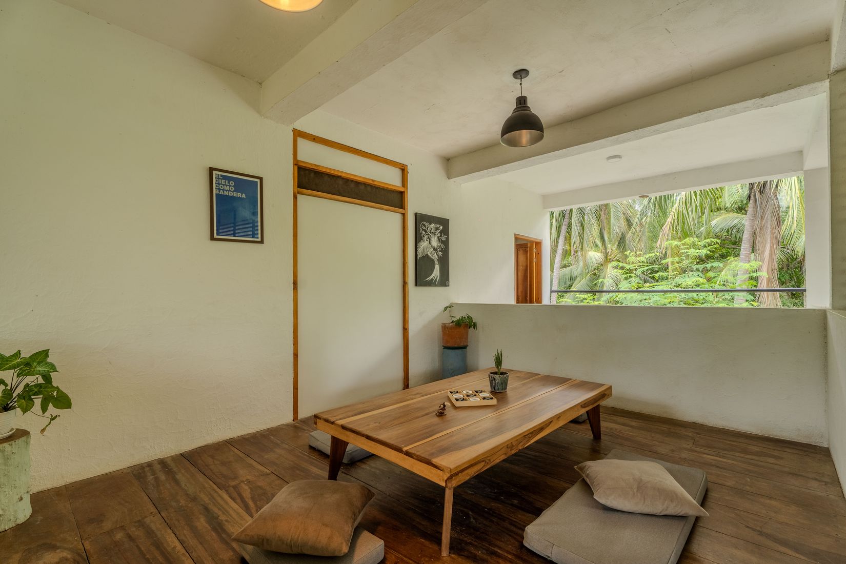 Sala de estar con cojines en el piso, una mesa de madera baja y vista al jardín tropical.