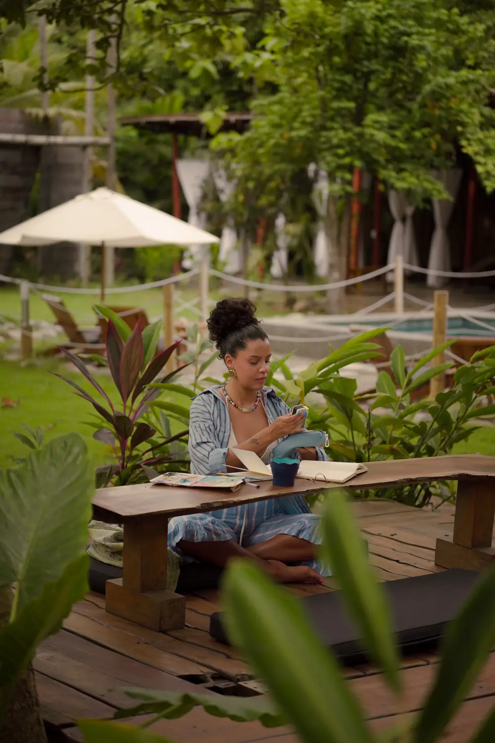 Yeraldina sentada en una banca de madera en el jardín de Casa Chapolín, dibujando en su bitácora.